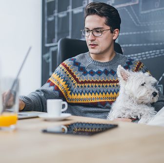 Man working in the office and holding his liitle dog.